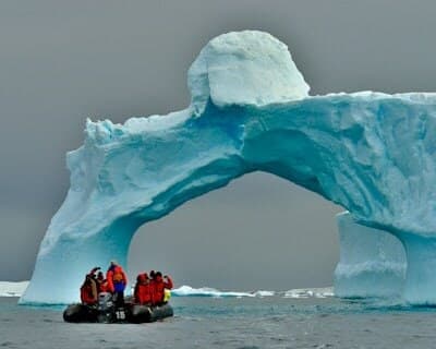 Une arche de glace au-dessus de la mer, un canot pneumatique chargé de passagers à ses pieds